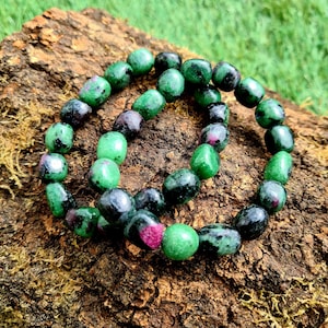 May include: Two green and black gemstone bracelets with pink accents. The bracelets are made of round, smooth stones and are stacked on top of each other.