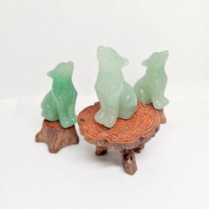 Könnte beinhalten: Drei grüne Jade-Wolf-Figuren auf Holzsockeln. Die Wölfe sitzen aufrecht mit erhobenem Kopf. Die Sockel sind aus Holz und haben eine natürliche Oberfläche.