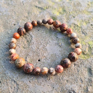 Può includere: Un braccialetto fatto di perline con motivi marroni, bianchi e arancioni con accenti dorati.