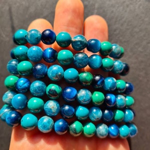 Puede incluir: Pila de pulseras de piedras preciosas azules y verdes. Las pulseras están hechas de cuentas redondas y están apiladas unas sobre otras.