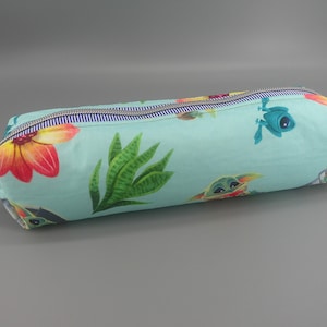 May include: A cylindrical pencil case with a light blue background, featuring a colorful floral and character pattern. The design includes red, orange, and yellow flowers, green plants, and cartoon characters. A zipper runs along the top, and a beige fabric loop is attached to the side.