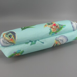 May include: A light blue, rectangular pillow featuring a repeating pattern of a cartoon character and space-themed imagery. The pillow has a beige fabric loop attached to one end.