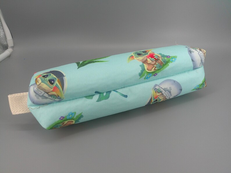 May include: A light blue, rectangular pillow featuring a repeating pattern of a cartoon character and space-themed imagery. The pillow has a beige fabric loop attached to one end.