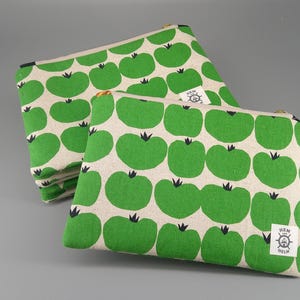 May include: Two canvas zipper pouches with a repeating pattern of green apple shapes on a cream background. The pouches are different sizes and are stacked. One pouch has a small white tag that says "HEM for HELM".