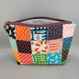 May include: A zippered pouch made of colorful patchwork fabric featuring various patterns including tigers, fish, flowers, and checkered squares. A white rectangular label with the text HEM AND HELM and a ship wheel icon is centered on the front.