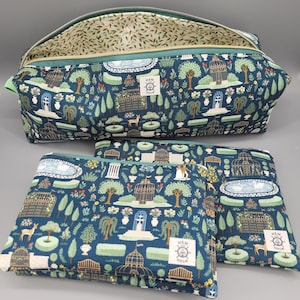 May include: A set of three dark blue zippered pouches featuring a repeating garden print with fountains, gazebos, trees, and deer. Each pouch has a small white rectangular label with the text HEM AND HELM and a ship wheel logo on the front.
