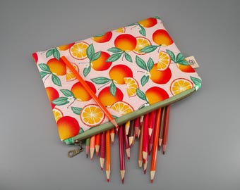May include: A pencil case with a light pink background and a pattern of oranges and orange slices. The case is open, revealing a collection of colored pencils in shades of red, orange, and purple. An orange pencil rests on top.