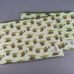 May include: Two rectangular fabric zipper pouches featuring a repeating pattern of small green creatures with large ears and brown robes on a light green background. Each pouch has a small white square label with a ship wheel and the text Hem and Helm.