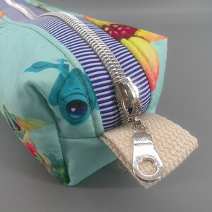 May include: A rectangular pencil case with a silver zipper and a beige fabric pull tab. The case features a light blue fabric with a colorful floral and sea creature pattern. A blue and white striped fabric is sewn near the zipper.