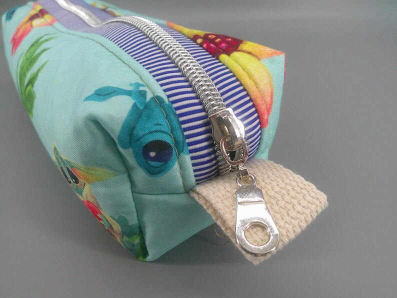 May include: A rectangular pencil case with a silver zipper and a beige fabric pull tab. The case features a light blue fabric with a colorful floral and sea creature pattern. A blue and white striped fabric is sewn near the zipper.
