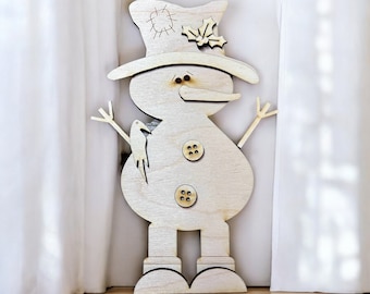 May include: A wooden snowman decoration with a top hat, twig arms, and a bird. The snowman has button eyes and a carrot nose. Two wooden buttons are on the snowman's belly. The snowman is made of light-colored wood.