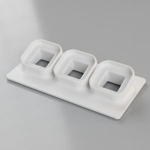 Può includere: Stampo in plastica bianca con tre tagli quadrati. Lo stampo è progettato per realizzare piccoli dolcetti quadrati.