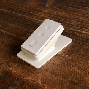 May include: A white Wemo smart switch with three buttons. The switch is on a white stand.
