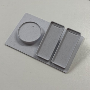 May include: A light grey, speckled, plastic desk organiser with a rectangular base, a circular holder, and two rectangular trays. The organiser is designed to hold various office supplies.