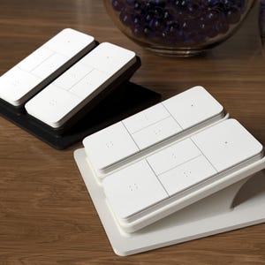 May include: White rectangular electronic devices with multiple buttons are stacked on black and white bases. The devices are on a wooden surface, with glass bowls of decorative marbles in the background.