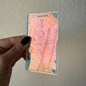 May include: A rectangular iridescent badge featuring a line art illustration of a CT scanner, a caduceus symbol, and two hands. The text THE CT TECH is printed at the bottom. The badge has a slot at the top for a lanyard and displays a shifting holographic color effect.