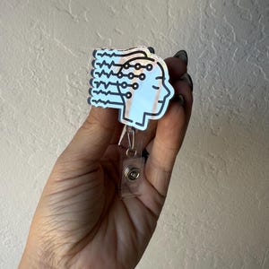 Peut inclure: Un badge blanc et noir représentant un profil de tête avec un design de circuit imprimé. Le badge est doté d'une lanière en plastique transparent et d'un clip en métal. Le design est d'une esthétique moderne et inspirée de la technologie.