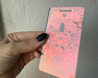 Puede incluir: Un inserto rectangular holográfico para porta credenciales con un diseño de carta de tarot. El gráfico muestra a una persona de enfermería en un marco de corazón con el texto "CHARGE NURSE" en la camisa y "THE CHARGE NURSE" abajo, rodeado de motivos florales.