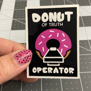 May include: A black and white sticker with a pink donut with white sprinkles and the text "Donut of Truth Operator".