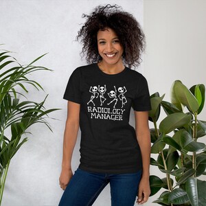 May include: Black t-shirt with a white graphic of dancing skeletons and the text "Radiology Manager". The short-sleeved shirt is made of a soft material.
