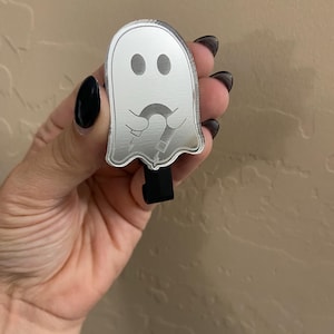 May include: A silver ghost-shaped keyring with a black clip. The ghost has a sad face and is holding a candy cane.