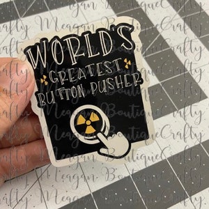May include: A black and white sticker with the text "World's Greatest Button Pusher" and a yellow and black radiation symbol with a hand pointing at the button.