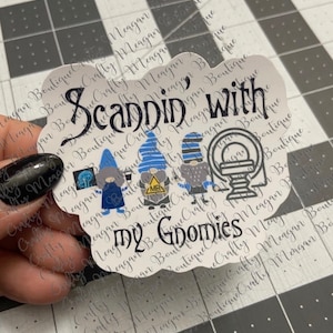 May include: A white sticker with a cloud-shaped outline. The sticker features a black and white illustration of four gnomes with blue hats and a black and white MRI machine. The text "Scandin' with my Gnomies" is written in black.