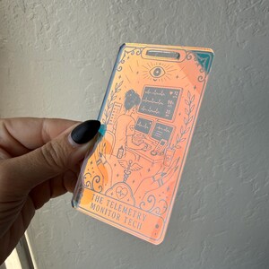 May include: A rectangular holographic badge featuring an illustration of a telemetry monitor technician working at a desk with computer screens displaying heart rhythms. The text THE TELEMETRY MONITOR TECH is printed at the bottom of the badge.