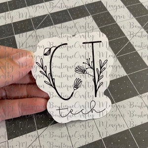 May include: A black and white sticker with the letters "CT" in a stylized font with floral accents. The word "tech" is written below the letters.