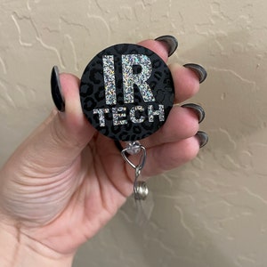 May include: A black retractable badge reel with the text "IR TECH" in silver glitter. The reel has a leopard print design and a clear plastic clip. The badge reel is a useful accessory for anyone who needs to display an ID badge.