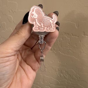 May include: A rose gold retractable badge holder with a cartoon skeleton dog design.