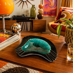 May include: A crescent-shaped ashtray featuring a glossy black exterior and a vibrant, textured turquoise centre. The piece has a wide, curved basin with integrated cigarette rests along the edges, showcasing a smooth, reflective finish throughout.