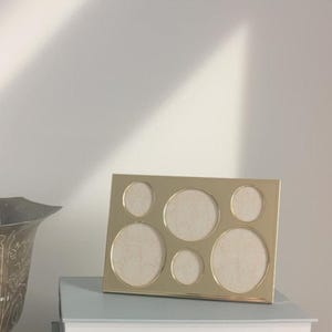 May include: A gold-toned metal picture frame with six circular openings for photos. The frame is sitting on top of two books.