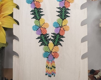 May include: A colorful beaded necklace and matching earrings with a floral design. The necklace features a series of multi-colored flowers with green leaves, and a tassel at the bottom. The earrings are also floral shaped with a tassel.