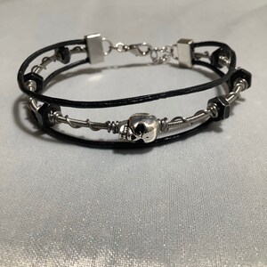 May include: A black leather choker with a silver skull charm, accented with silver wire and black metal beads.