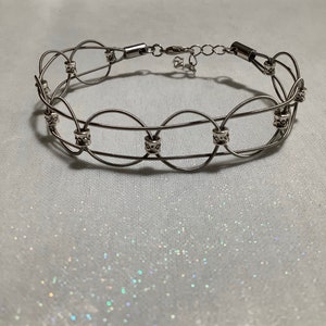 May include: A silver wire choker necklace with decorative silver beads. The necklace has a clasp closure.