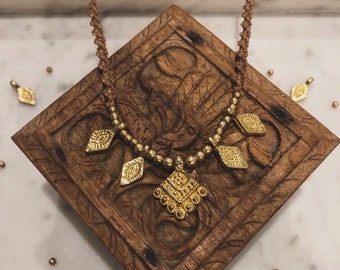 May include: A gold necklace with a geometric pendant and smaller diamond-shaped charms. The necklace is made of brown cord and gold beads.