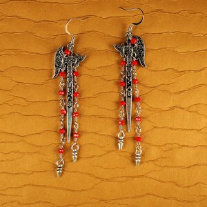 May include: A pair of silver dangle earrings with red beads and a sword-like design. The earrings have a detailed, ornate design.