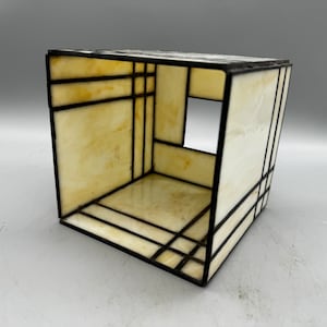 May include: A small, cube-shaped stained glass lampshade with a white and black geometric design. The lampshade is made of clear glass with black lines and a white interior.