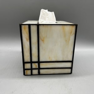 May include: A white tissue box cover with a geometric design in black. The cover is made of stained glass and has a white background with black lines.