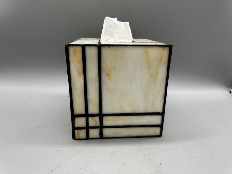 May include: A white tissue box cover with a geometric design in black. The cover is made of stained glass and has a white background with black lines.