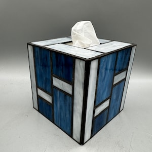 May include: A blue and white stained glass tissue box cover. The box is square and has a geometric pattern.