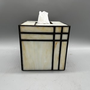 May include: A white tissue box cover with a geometric design made of black stained glass.