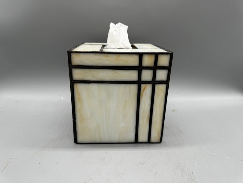 May include: A white tissue box cover with a geometric design made of black stained glass.