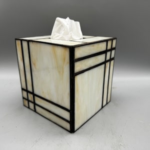 May include: A white and cream stained glass tissue box cover with black geometric lines.