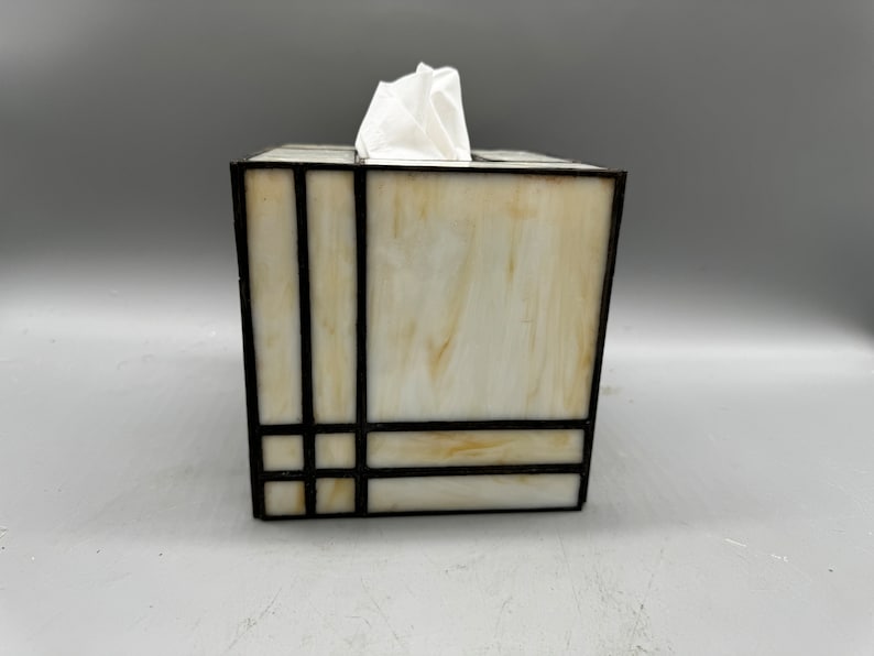 May include: A white tissue box cover with a geometric design in black stained glass.