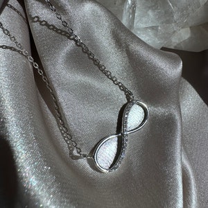 Peut inclure: Un collier infini en argent avec un design de cristal clair scintillant. Le collier est présenté sur un fond en tissu doux gris clair.