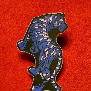 May include: A blue and black sticker of a tiger with pink eyes. The tiger is standing on its hind legs and has a black background. The sticker has the word "INGRAE" written on it.