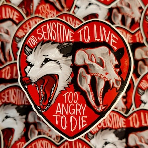 May include: A red heart-shaped sticker with a white opossum and a skull with the text "Too Sensitive to Live" and "Too Angry to Die".