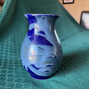 May include: A ceramic vase featuring a bulbous body and a flared rim, decorated with a marbled glaze pattern in shades of deep royal blue and light sky blue, creating a fluid, layered appearance across the smooth, glossy surface of the vessel.